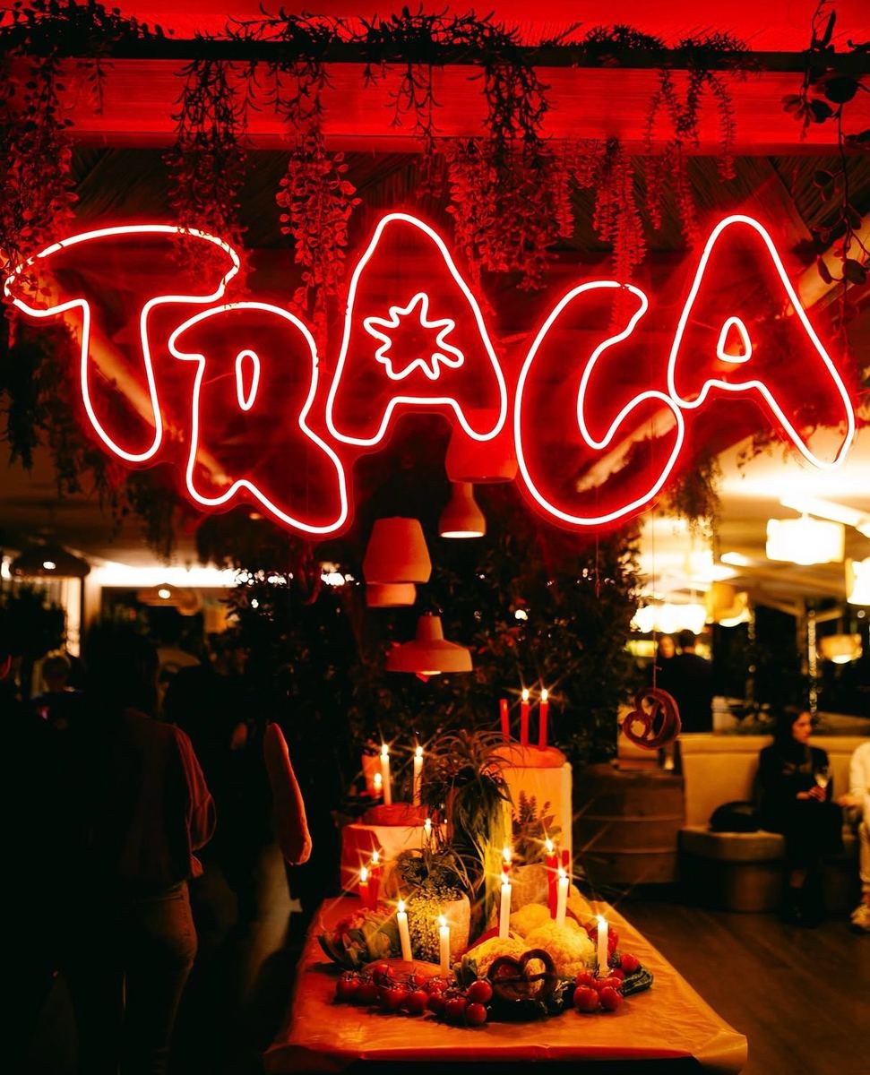 TRACA neon sign above a candlelit table at the opening